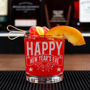 Red glass with 'Happy New Year's Eve' text, garnished with peach slices and a straw, on a bar counter.