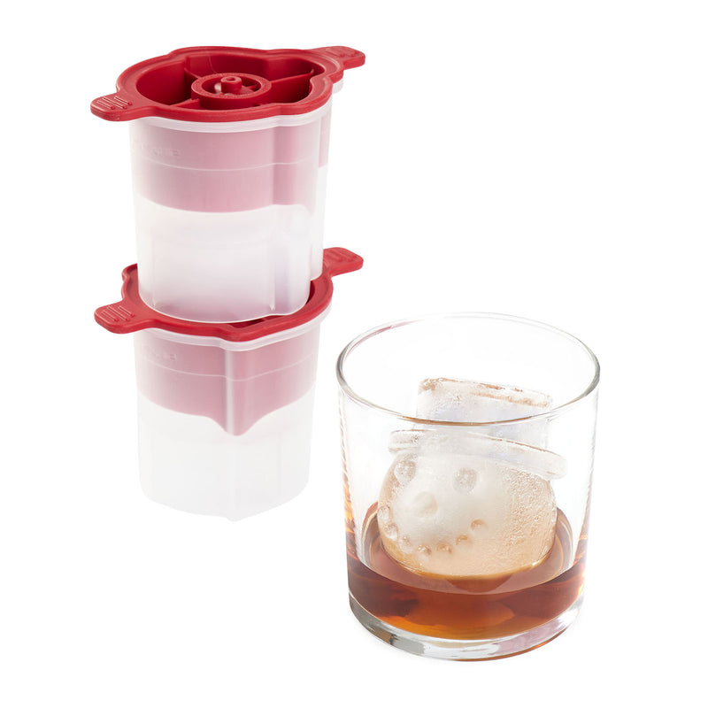 Red and white ice cube tray with a glass of liquid and ice cubes.