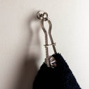 Metal towel hook on a white wall with a black towel draped over it.