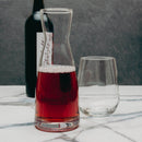 Glass carafe with red liquid and a wine glass on a marble surface