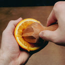 Person using a wooden orange squeezer to extract juice from an orange.