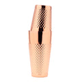 A polished copper cocktail shaker with a textured, diamond-patterned grip, shown stacked with two matching tumblers on a solid white background.