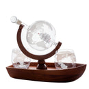 A glass decanter and two matching stemless glasses with an etched world map design, displayed on a dark wood boat-shaped tray with a matching wooden stand.