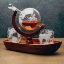 A glass globe decanter with a wooden stand and matching stemware, displayed on a wooden tray against a dark textured background.