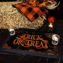 Halloween-themed decor with 'Trick or Treat' mat, candles, and fall elements on hay.