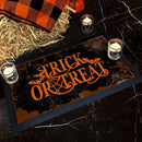 Halloween-themed doormat with 'Trick or Treat' text, surrounded by candles and hay on a dark surface.