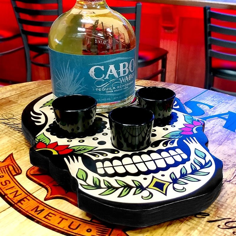 Cabo San Lucas tequila bottle with three black shot glasses on a decorative skull coaster.
