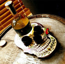Bottle of dark liquid with three shot glasses on a decorative skull-shaped tray.
