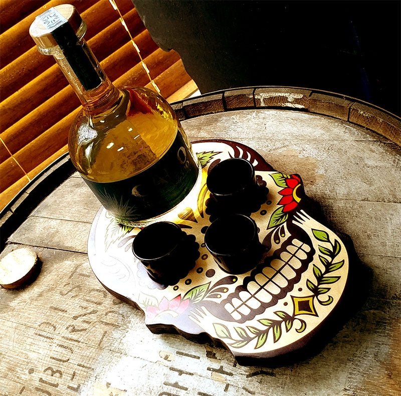 Bottle of dark liquid with three shot glasses on a decorative skull-shaped tray.