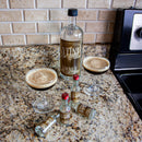 Bottle with custom label with two glasses of a dark beverage on a countertop and mini bottles with matching label. 