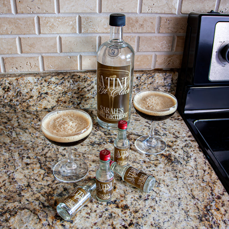 Bottle with custom label with two glasses of a dark beverage on a countertop and mini bottles with matching label. 